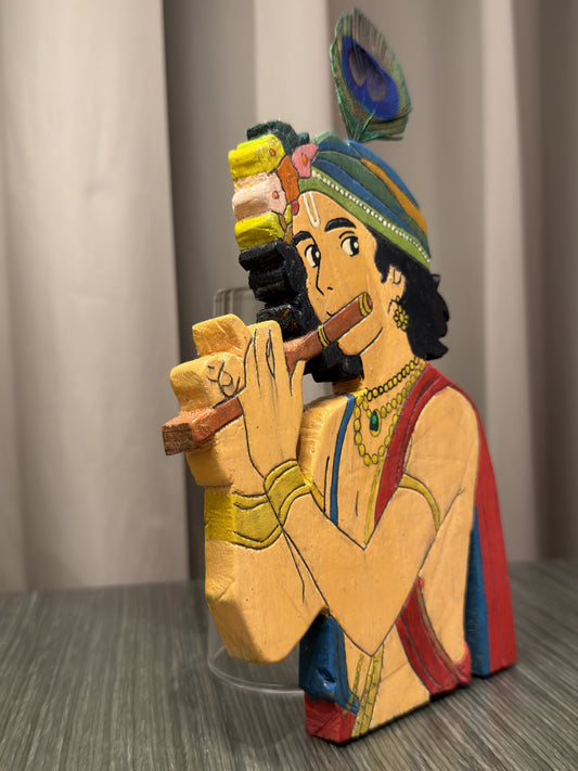 Close-up detail of hand-painted face, jewellery and flute on wooden Krishna figurine