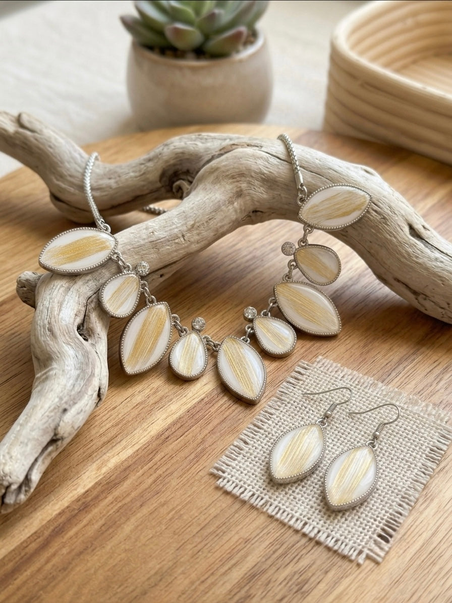 White and gold statement necklace draped on driftwood with matching earrings on jute cloth